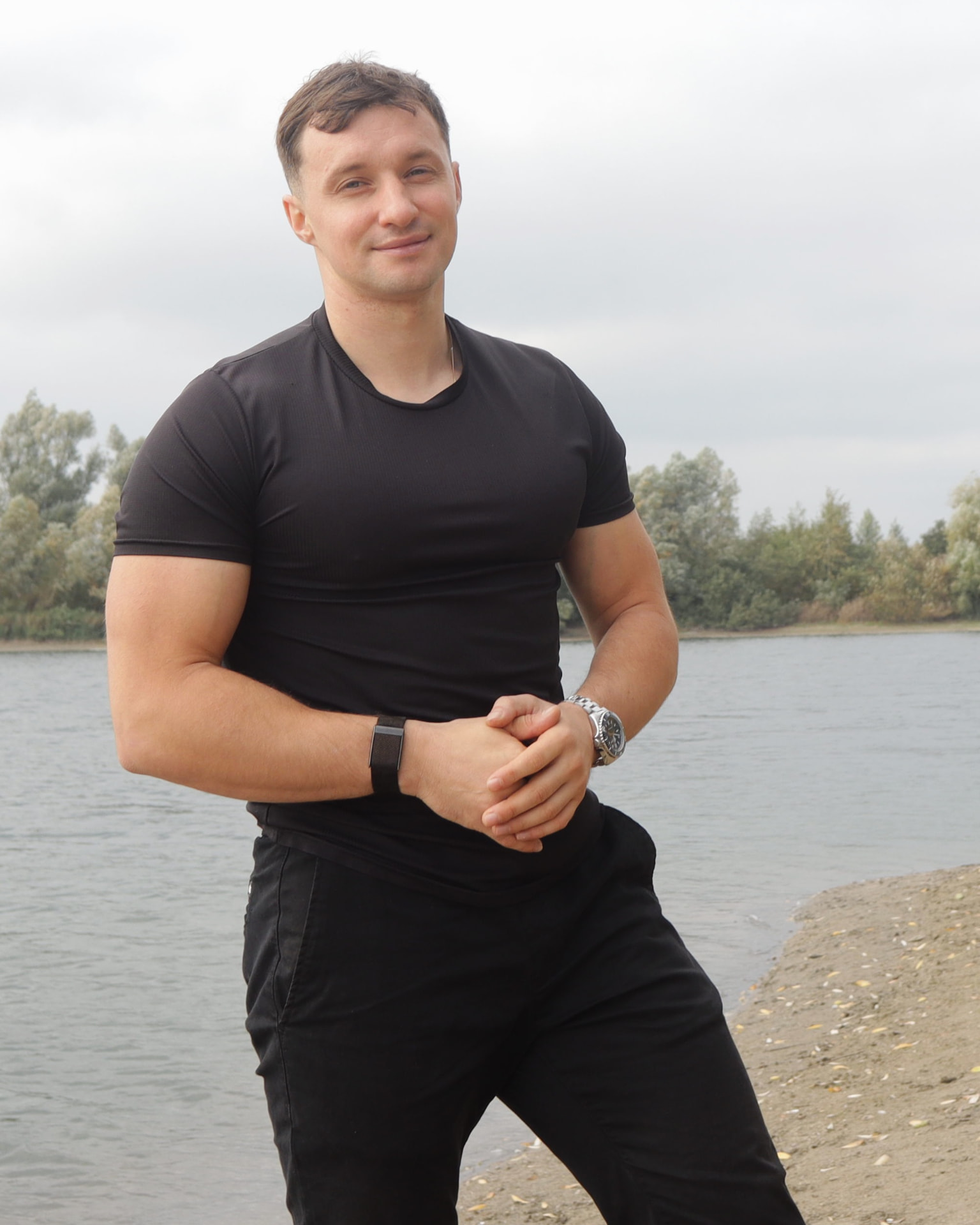 Deividas by a lake in natural sunlight, wearing a black T-shirt with his hands clasped